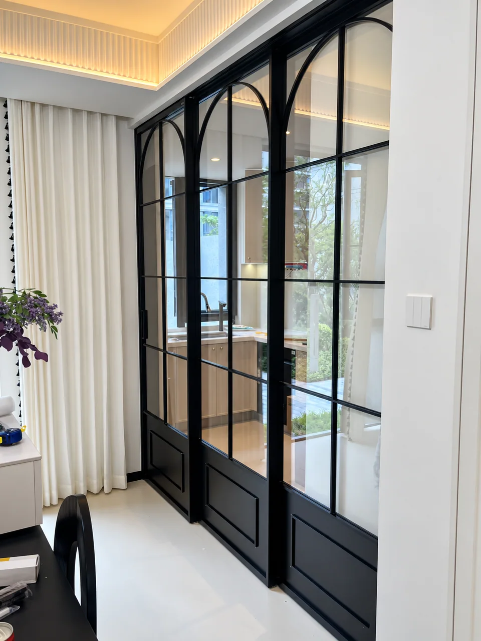 Black French sliding glass doors with arched grids separating a bright kitchen