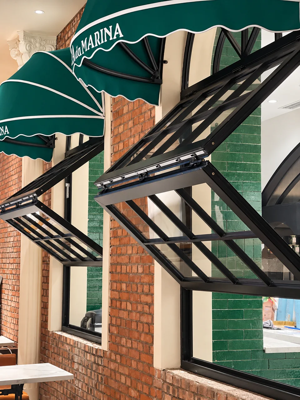 Black glazed bifold awning windows opened outward on a brick and tile storefront